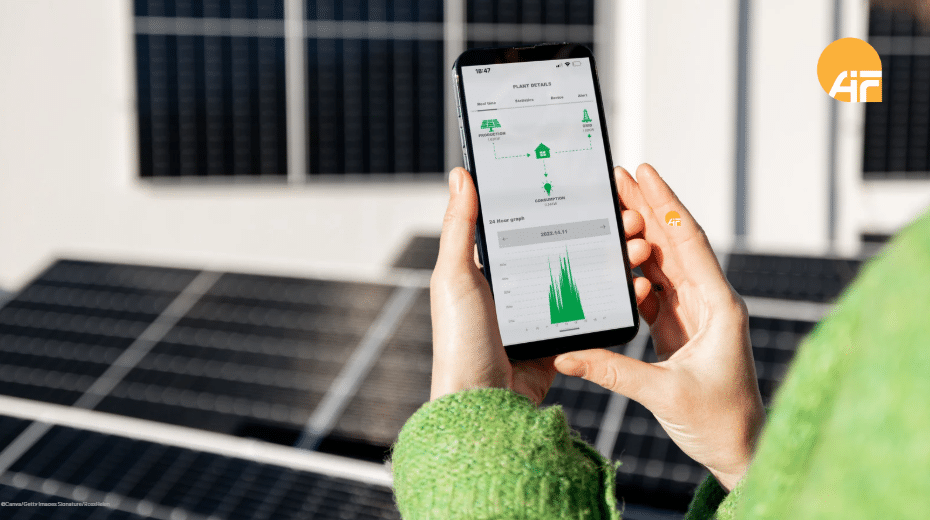 Eine Frau, die ein Handy mit einer App für Solaranlagen hält, steht vor einer Photovoltaikanlage.