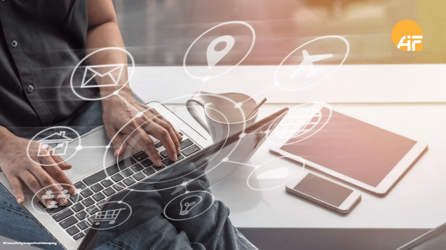 Ein Mann sitzt mit einem Laptop auf einem Tisch. Neben sich liegen Smartphone und Tablet.