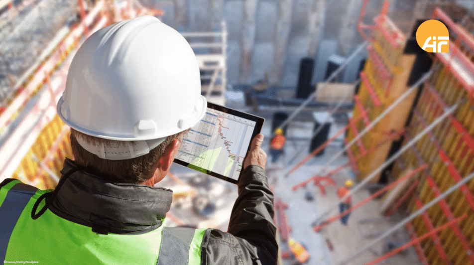 Ein Arbeiter mit einem Bauhelm und einem Tablet in der Hand. Im Hintergrund sieht man eine Baustelle.